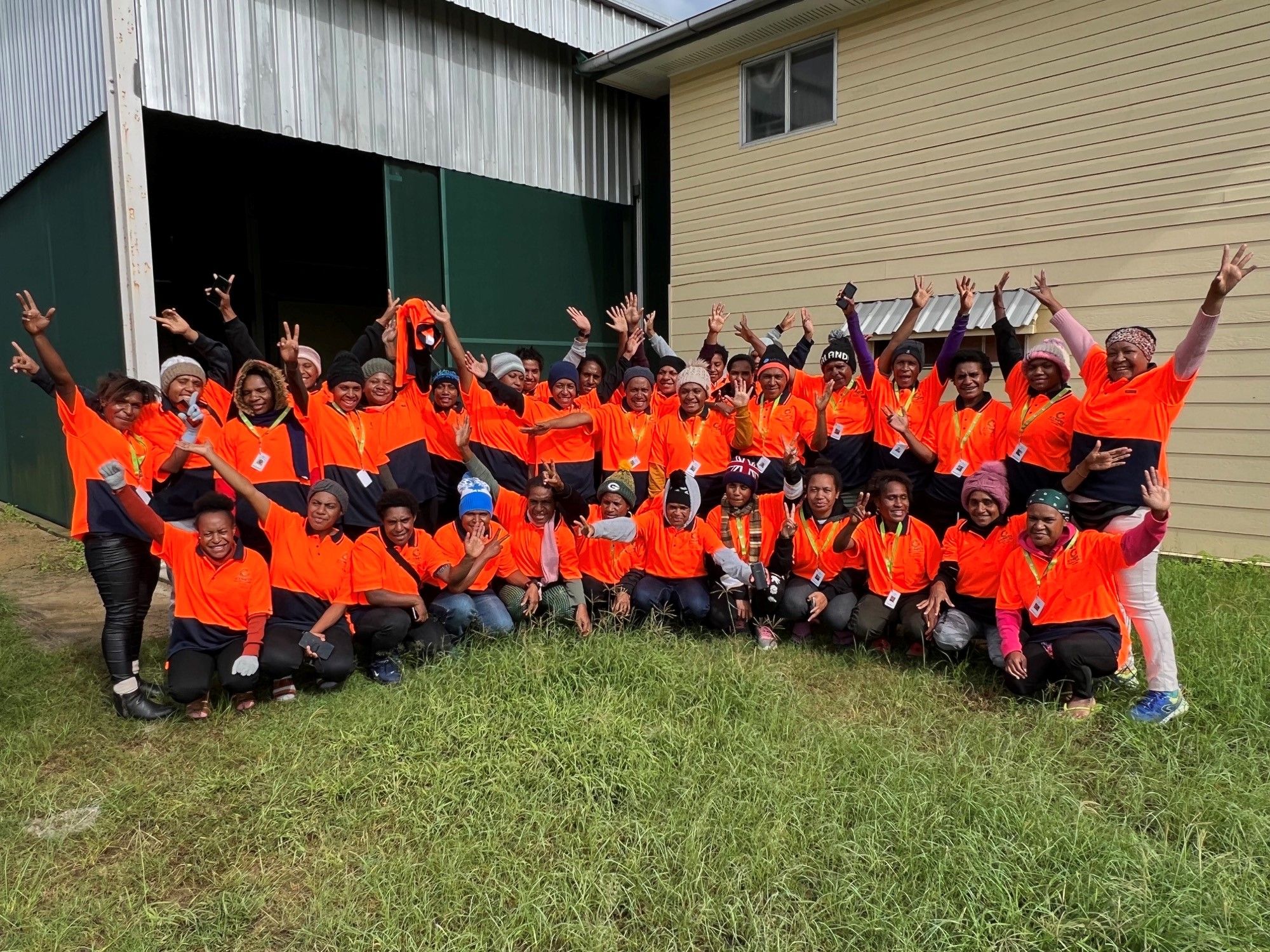 A group of women in workwear smiling and making celebratory gestures at a work site.