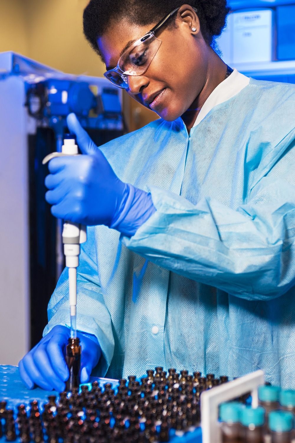 Lab technician dressed in personal protective equipment pipetting samples in a lab.